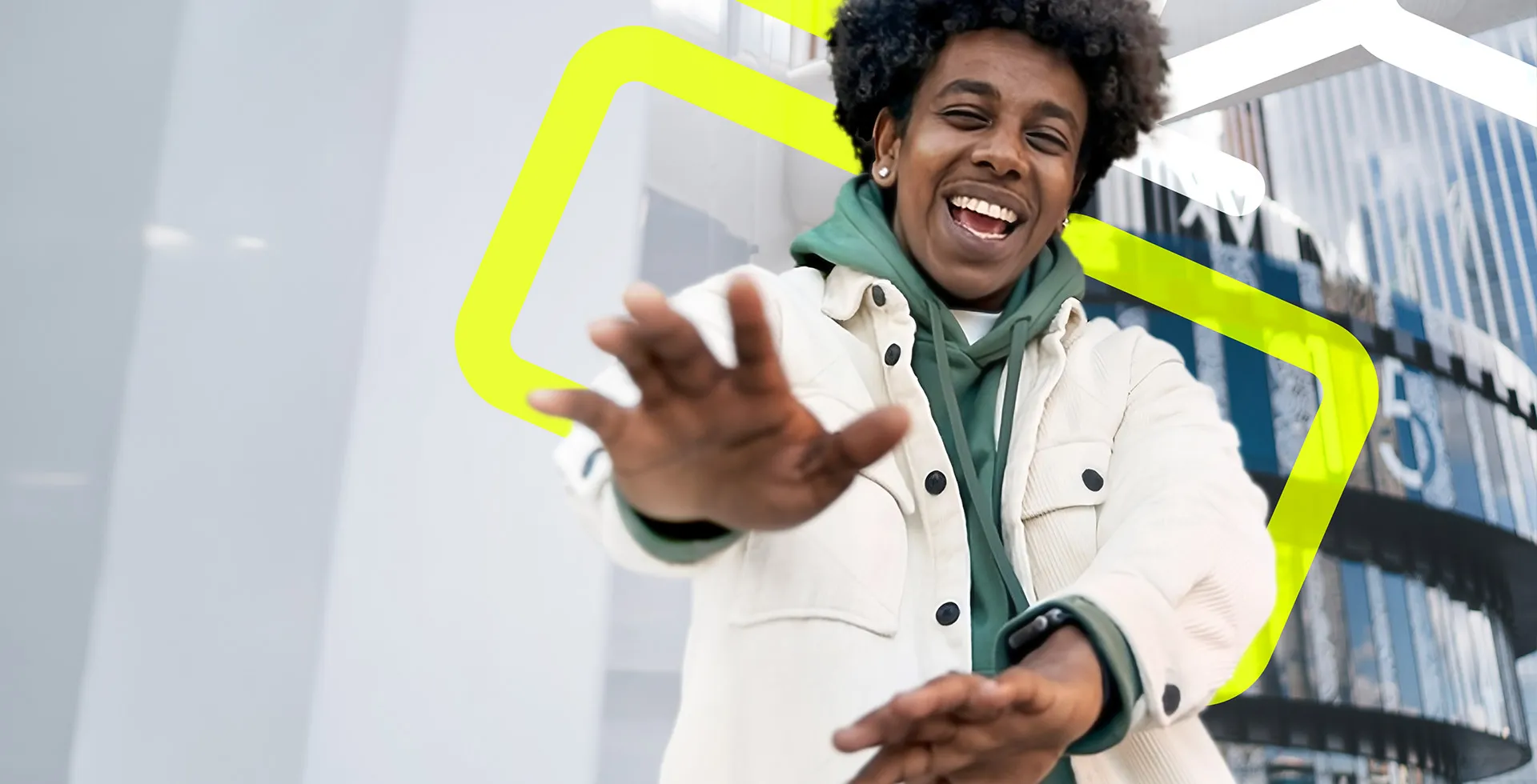 Young man with afro hair stood outside an office building holding his hands out as he smiles and laughs at the camera, happy about finding a HR role on TalentNext.	