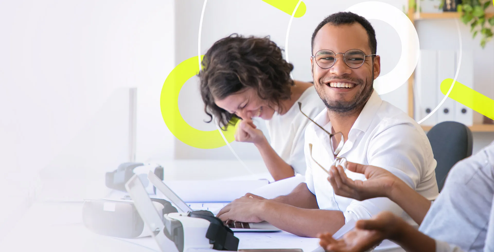 man sat between two colleagues at a desk smiling at the colleague on his left as they all laugh together, happy in the Tech role he found on the TalentNext platform.
